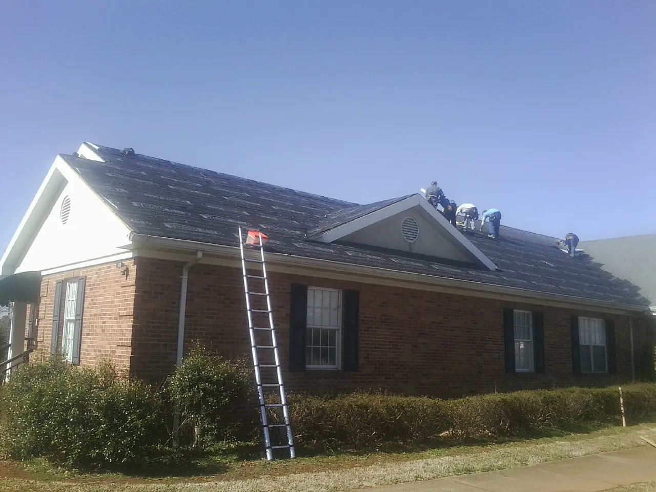 Crew tearing shingles off a brick ranch roof with a ladder set — Emergency Roof Repair work by our crew in Jamaica