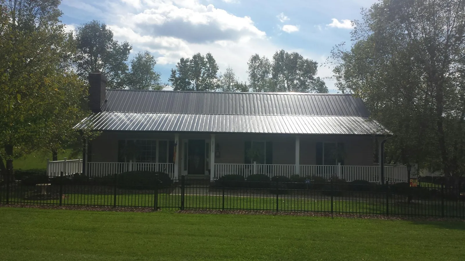 Gray metal roof on a brick ranch with a full width front porch — Gutter Guard Installation work by our crew in Jamaica