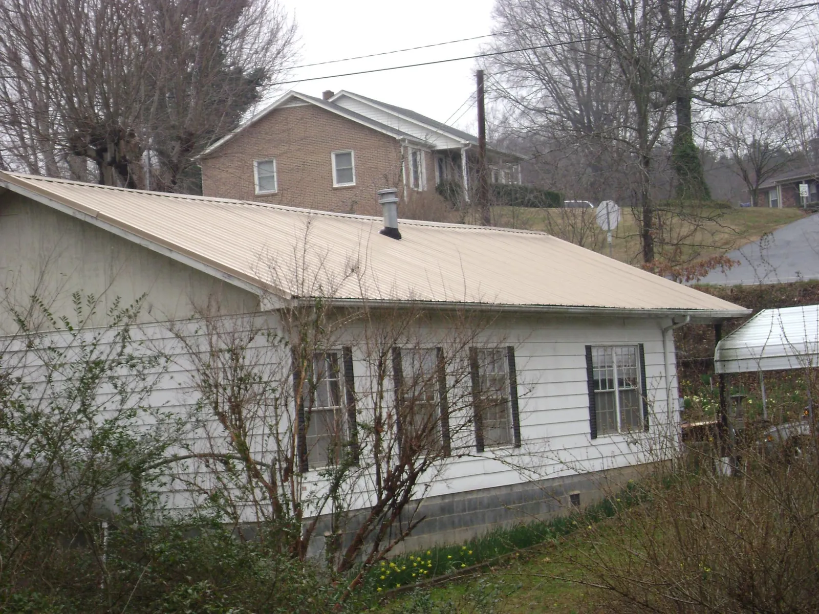 Tan metal roof on a white sided house set into a hillside — Commercial Roofing by Roofing Brothers in Jamaica